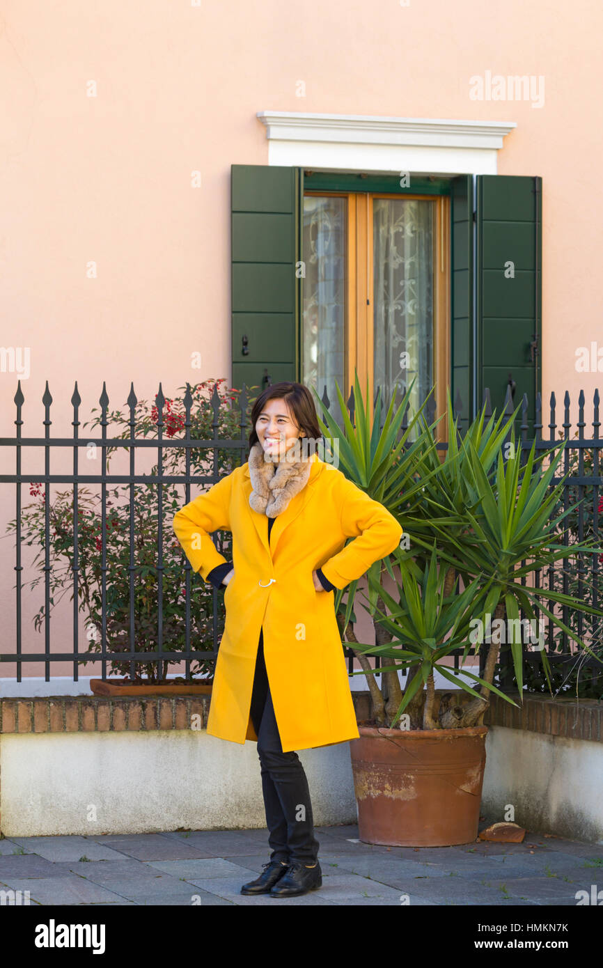 Female tourist posing for a photo in front of house at Burano, Venice, Italy in January Stock Photo