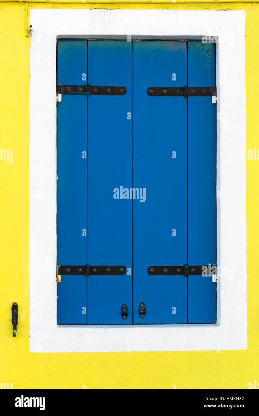 Blue window shutters contrast with yellow wall of house in Burano -  bright colors of Burano, Venice, Italy in January Stock Photo