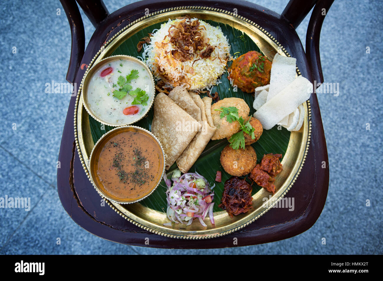 Close-up of Parsi Wedding thali with assorted dishes served on a round brass colored plate with banana leaf underliner placed on a wooden chair Stock Photo