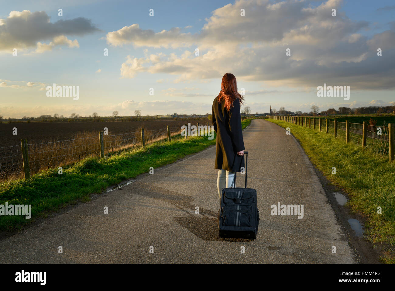 runaway girl standing with her suitcase on the road and look for the last time to her native village Stock Photo