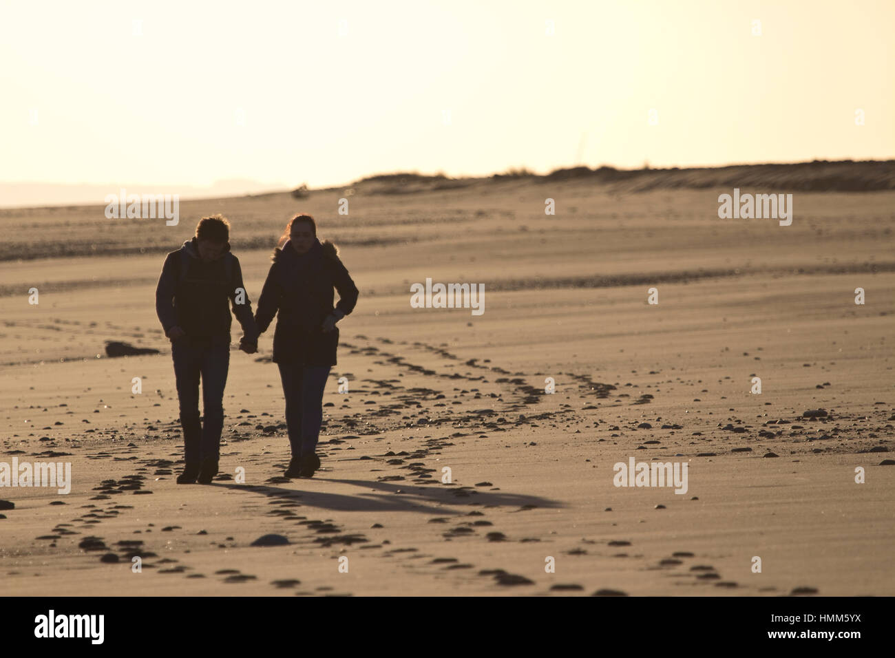 A young couple walking on a beach at dusk Stock Photo