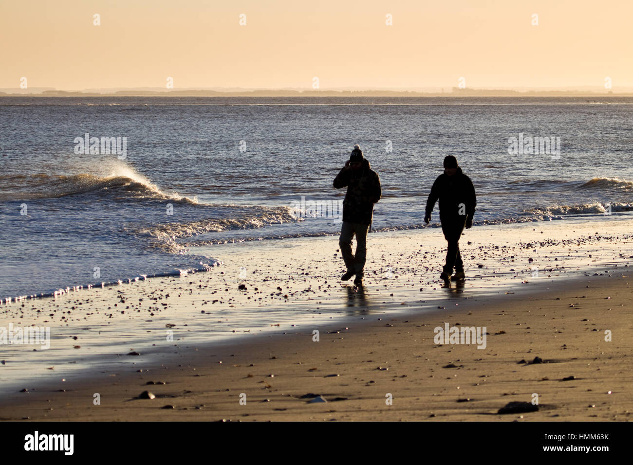 A young couple walking on a beach at dusk Stock Photo