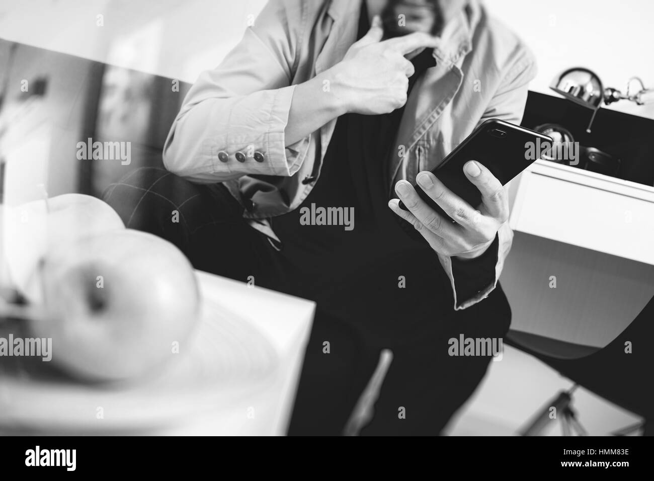 hipster hand using smart phone for mobile payments online business,sitting on sofa in living room,holding green apples in wooden tray,black and white Stock Photo