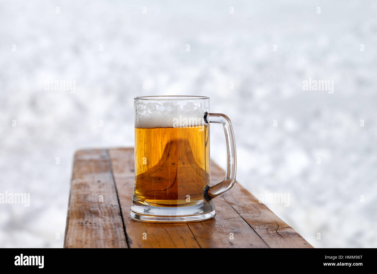 Glass mug with fresh cold beer on wooden bench in outdoor cafe at ski resort Stock Photo
