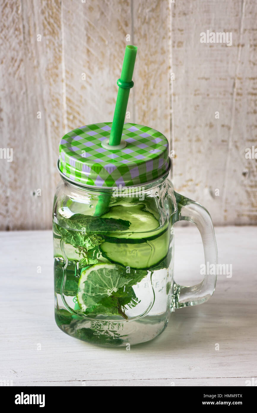 Mason jar mug with handle, lid and straw with detox cucumber agua fresca  water with lime and mint ingredients, on rustic wood kitchen table, spring  cl Stock Photo - Alamy