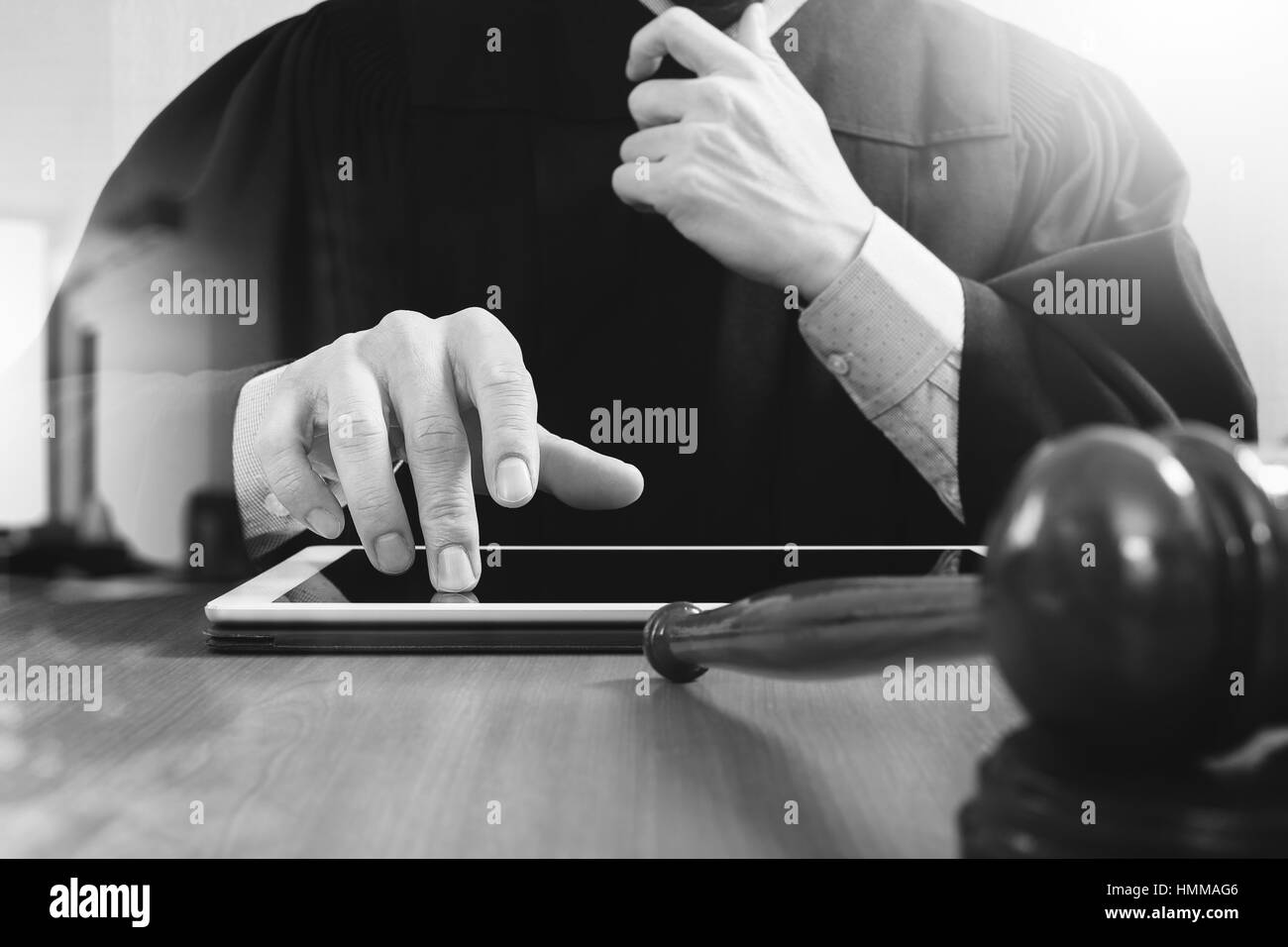 justice and law concept.Male judge in a courtroom with the gavel,working with digital tablet computer on wood table,black and white Stock Photo