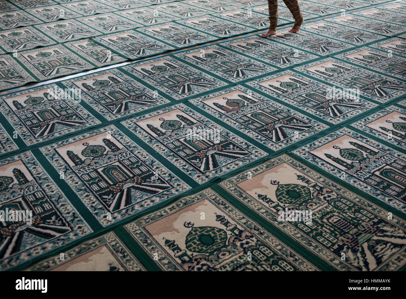 A person walks on top of Muslim praying carpets inside the Grand Mosque in Medan, Sumatra, Indonesia. Stock Photo