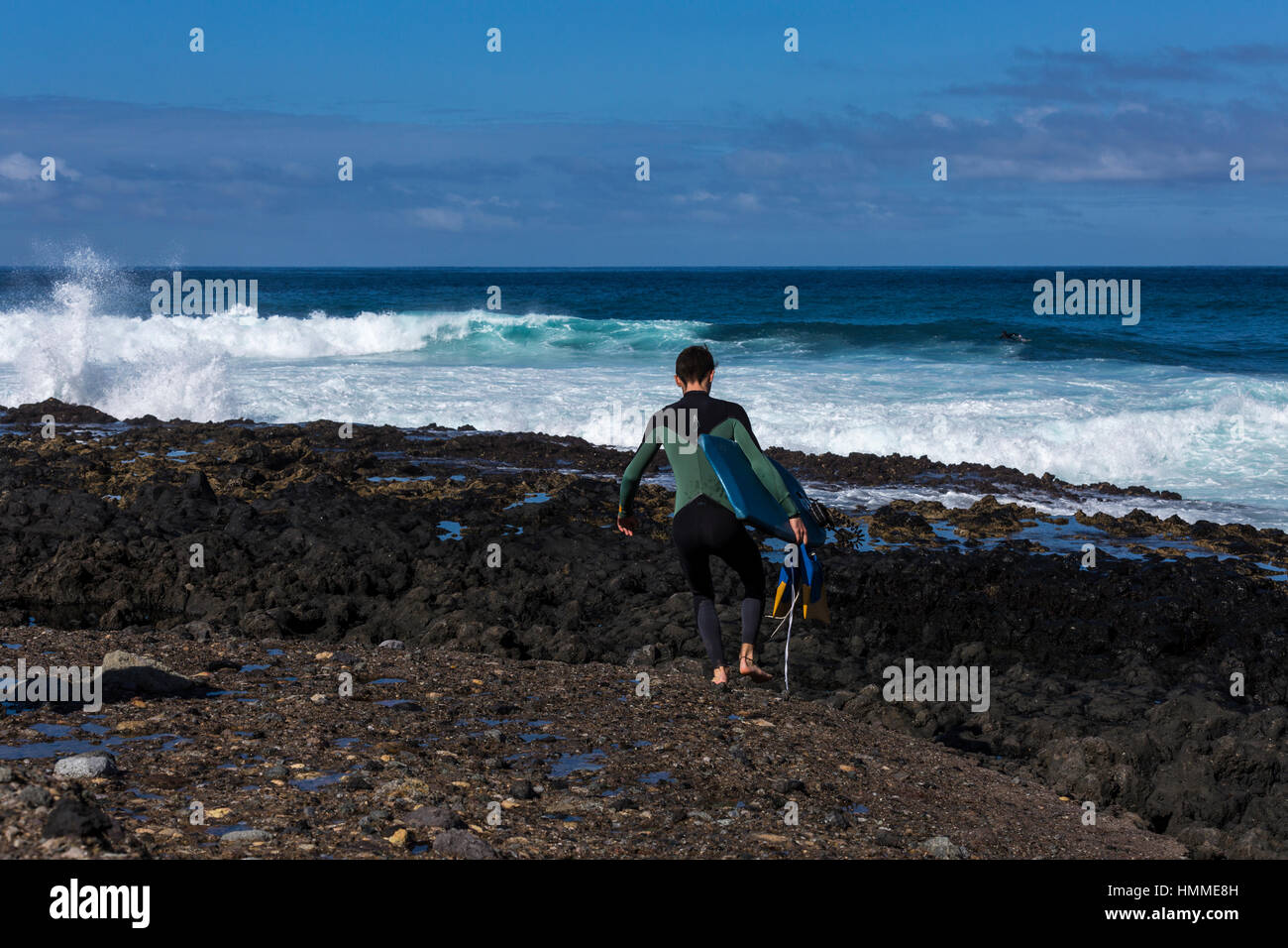 Bodyboarder crossing the rocks to enter the water at Punta Blanca in high waves on the west coast of Tenerife, Canary Islands, Spain Stock Photo
