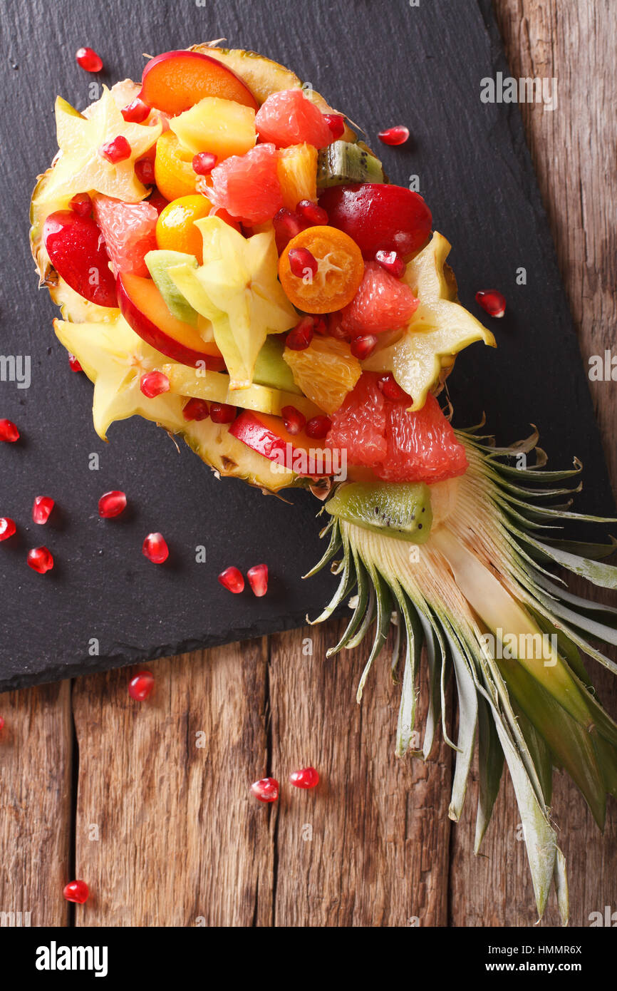 Salad of tropical fruit on a plate of pineapple close-up on the table. vertical view from above Stock Photo