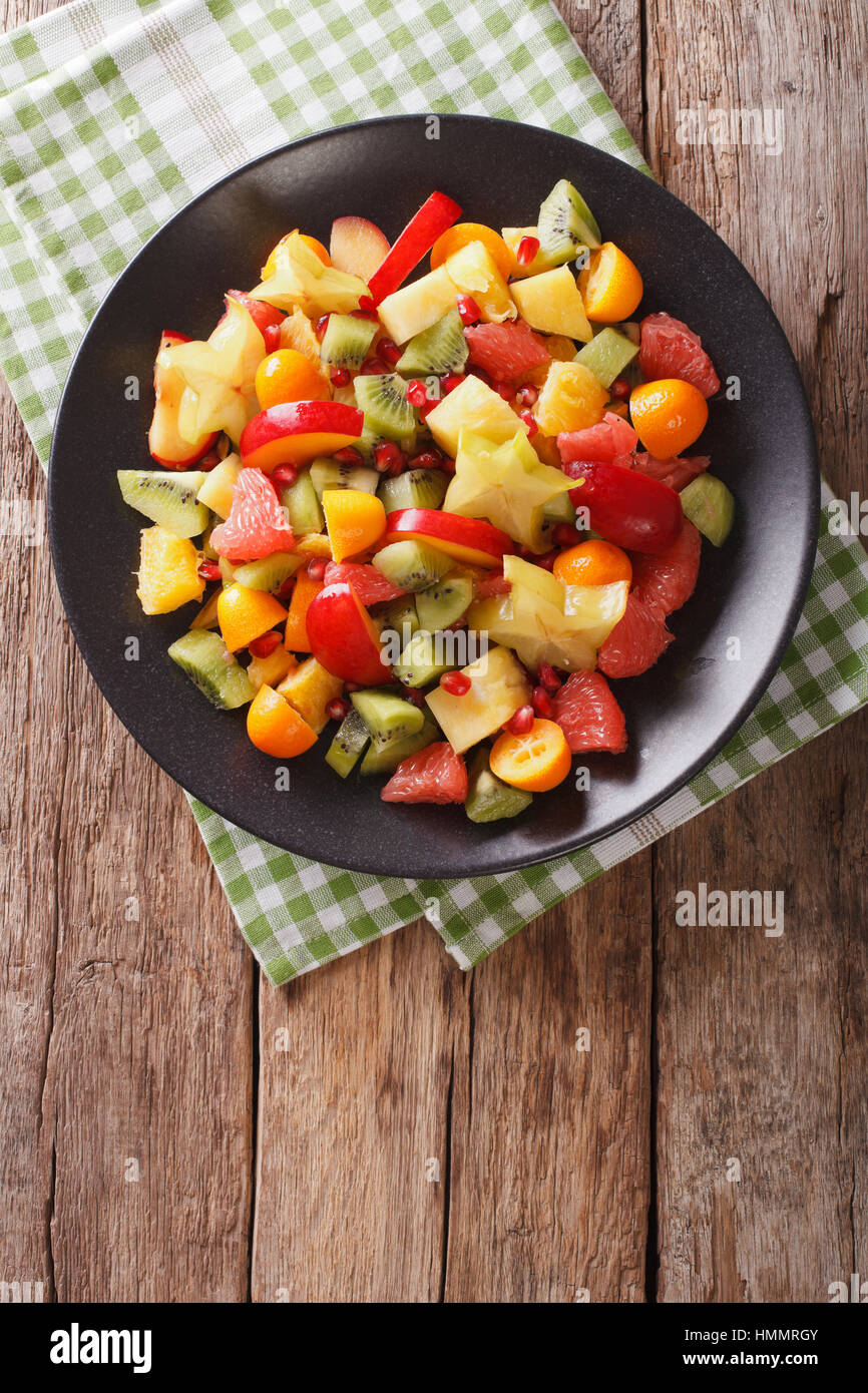 Fruit salad with orange, kumquat, pineapple, carambola, grapefruit, plum, pomegranate and kiwi close-up on a plate. vertical view from above Stock Photo