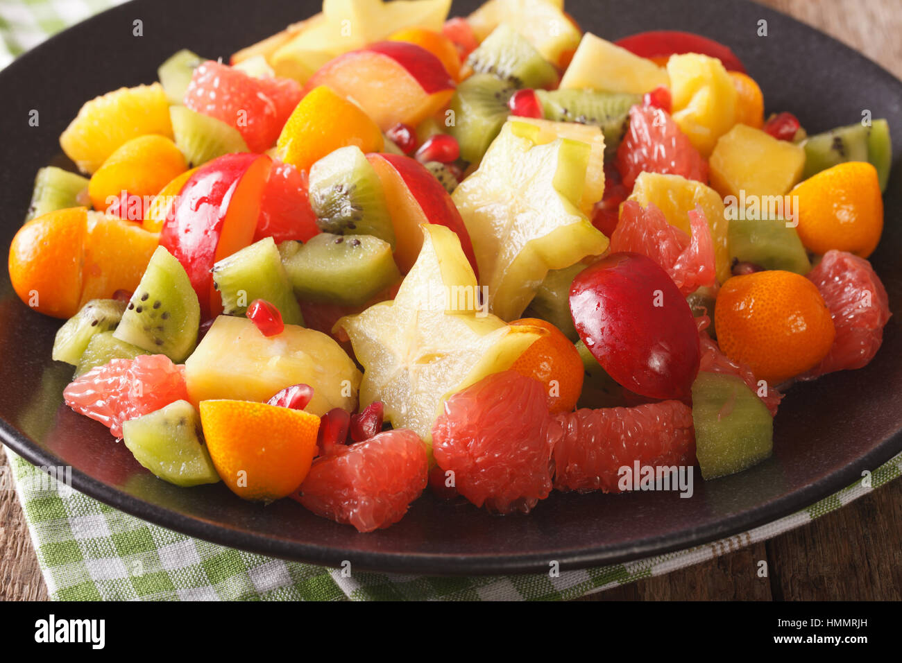 Fruit salad with orange, kumquat, pineapple, carambola, grapefruit, plum, pomegranate and kiwi close-up on a plate. horizontal Stock Photo