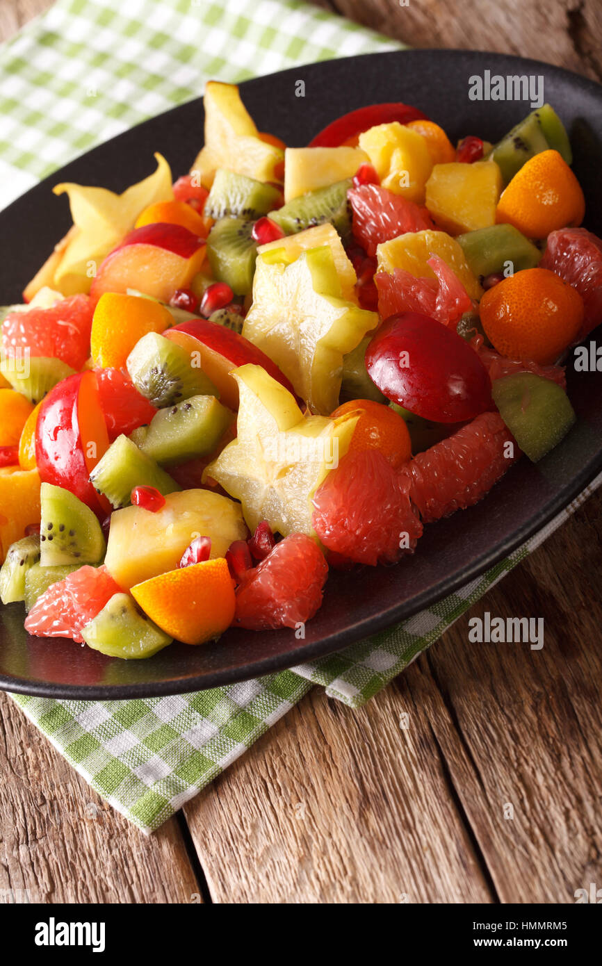 fruit salad of orange, kumquat, pineapple, carambola, grapefruit, plums and kiwi fruit close-up on a plate. vertical Stock Photo