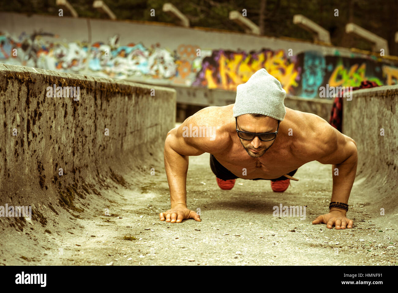 Slim fit elegant young adult man doing push up exercise outdoor in park ...