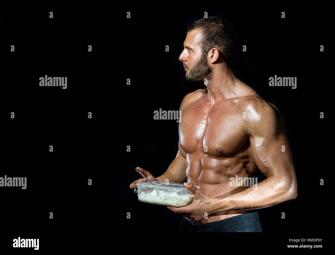 Young adult fit muscular bodybuilder eating healthy white rice from plastic dish isolated Stock