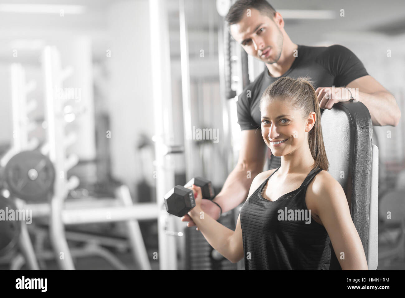 Young adult woman working out in gym, doing bicep curls with help of her personal trainer. Stock Photo