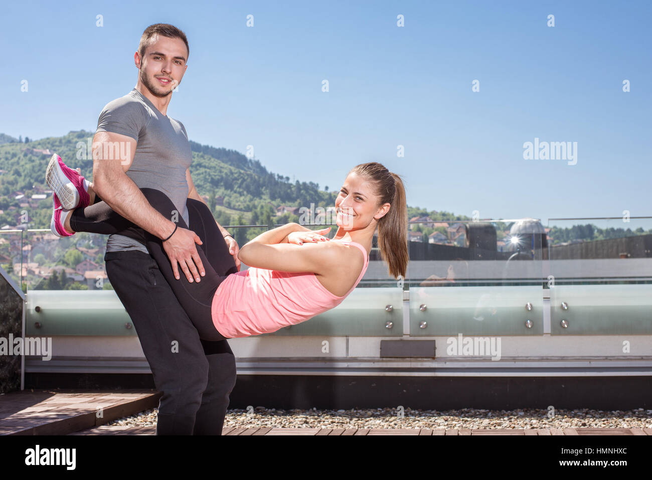 Young attractive couple doing advanced double dare crunches while standing on rooftop of the building in urban area. Stock Photo