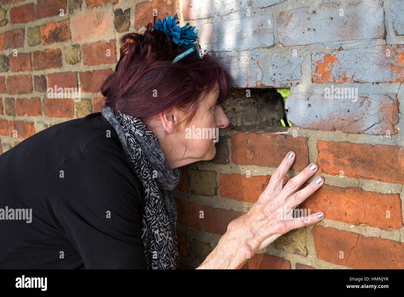 Woman looking through a hole in a brick wall Stock Photo