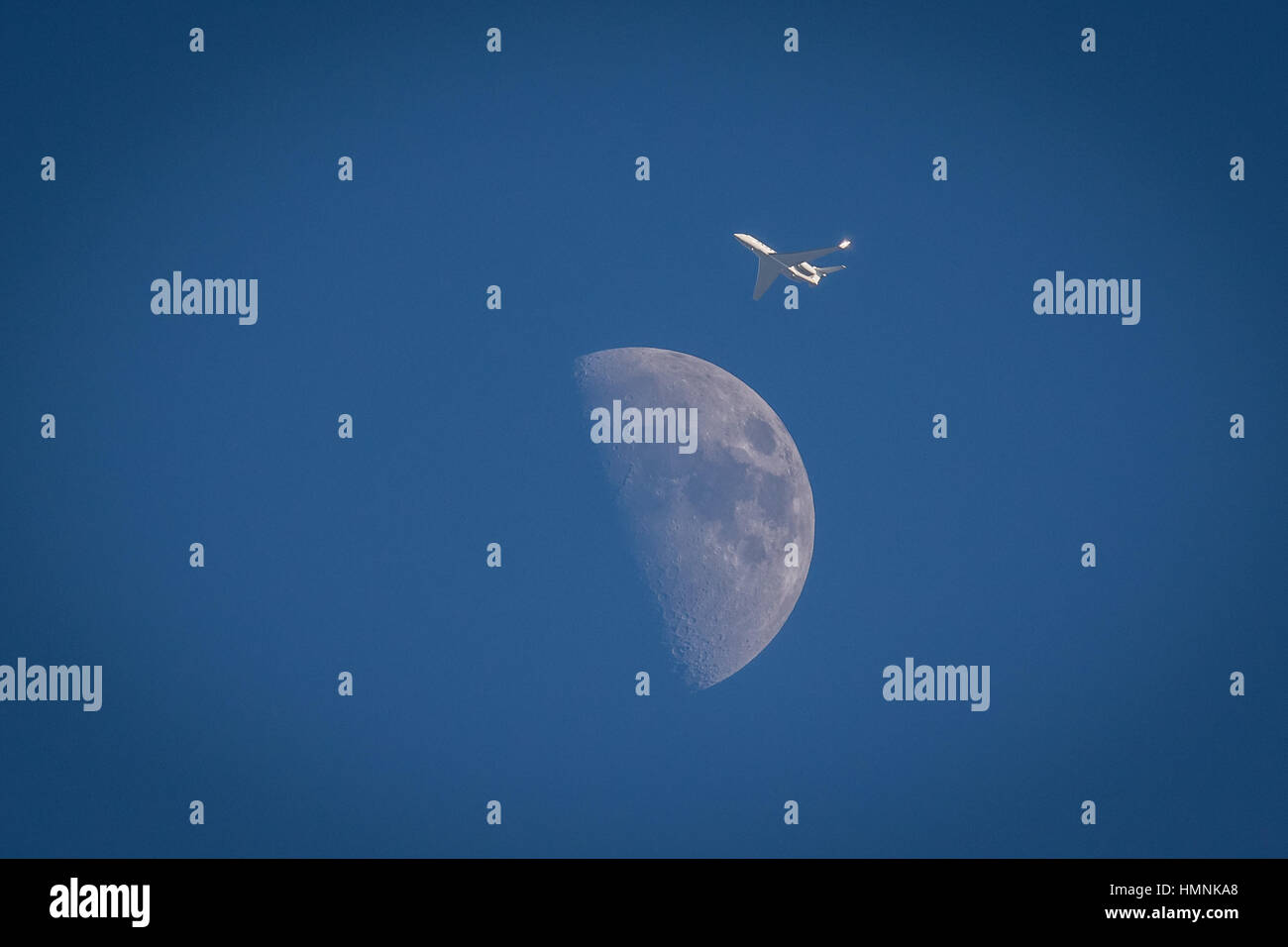 Image of a small private jet passing by the Moon on a sunny afternoon Stock Photo