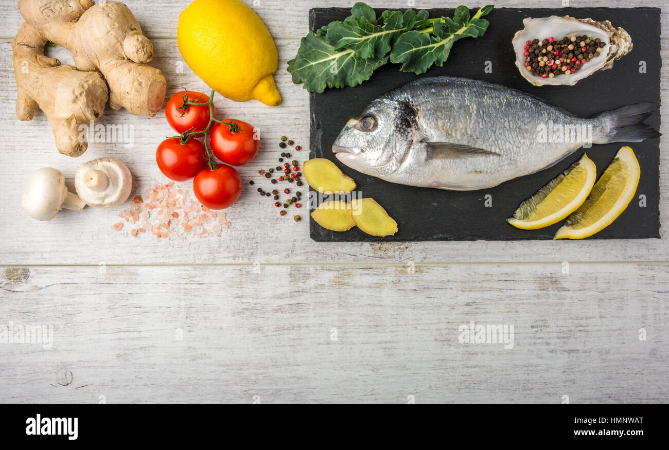 Useful dorado fish, rich in protein, vitamins, Omega 3 with vegetables, lemon and ginger, prepared for cooking on a white wooden table. Top view Stock Photo
