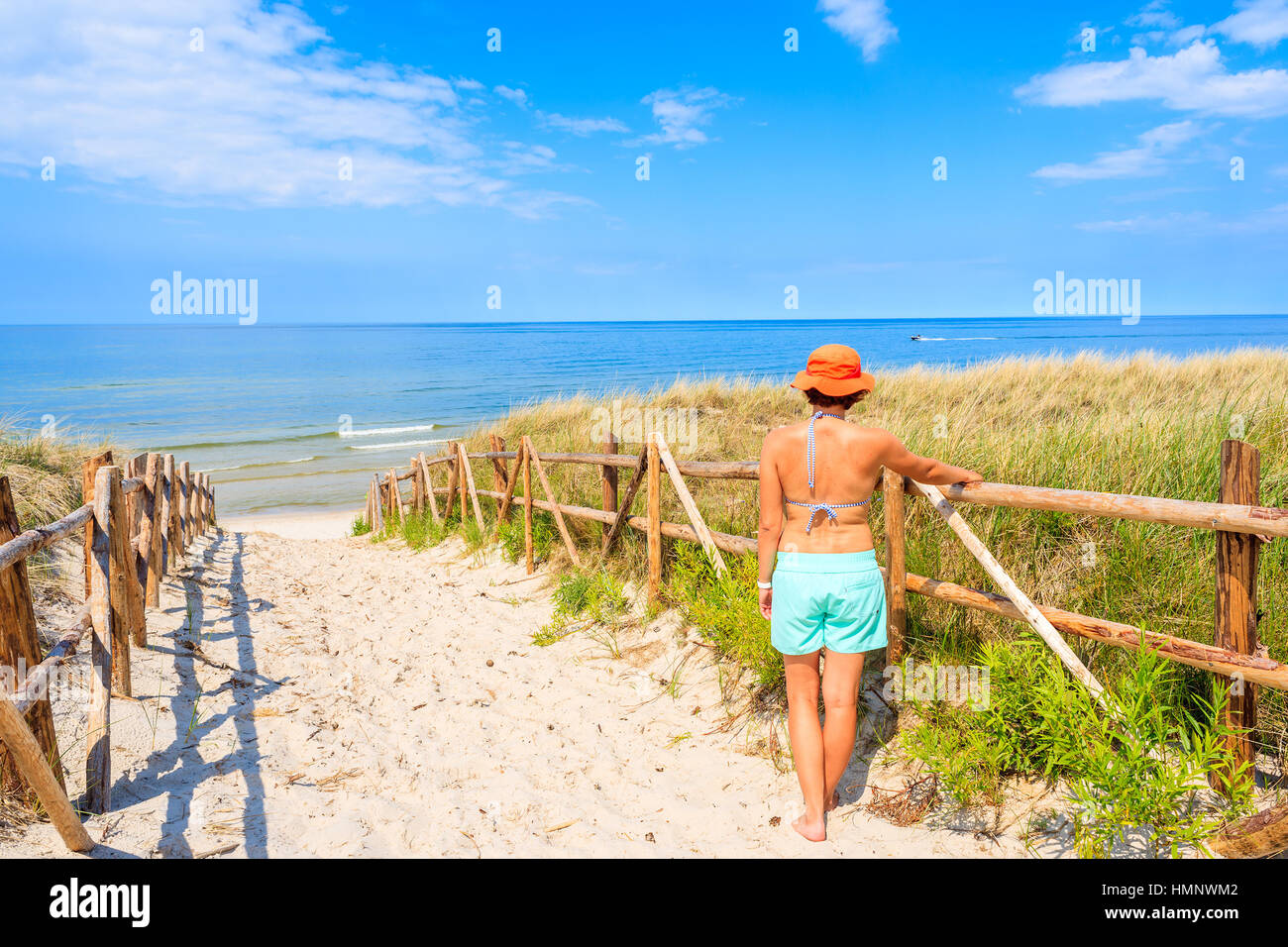 Young attractive woman standing by wooden fence of entrance to Lubiatowo beach, Baltic Sea, Poland Stock Photo