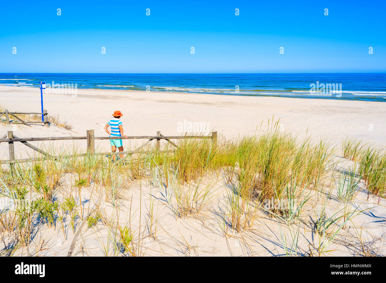 Young woman standing by wooden fence of entrance to beautiful Lubiatowo beach, Baltic Sea, Poland Stock Photo