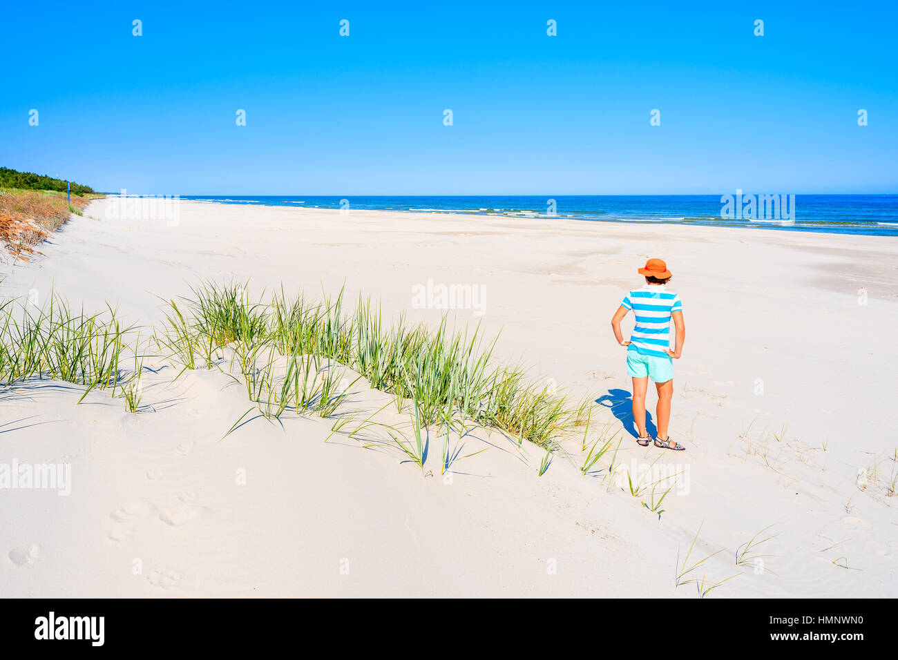 Young woman standing on white sand and looking at beautiful beach, Baltic Sea, Poland Stock Photo