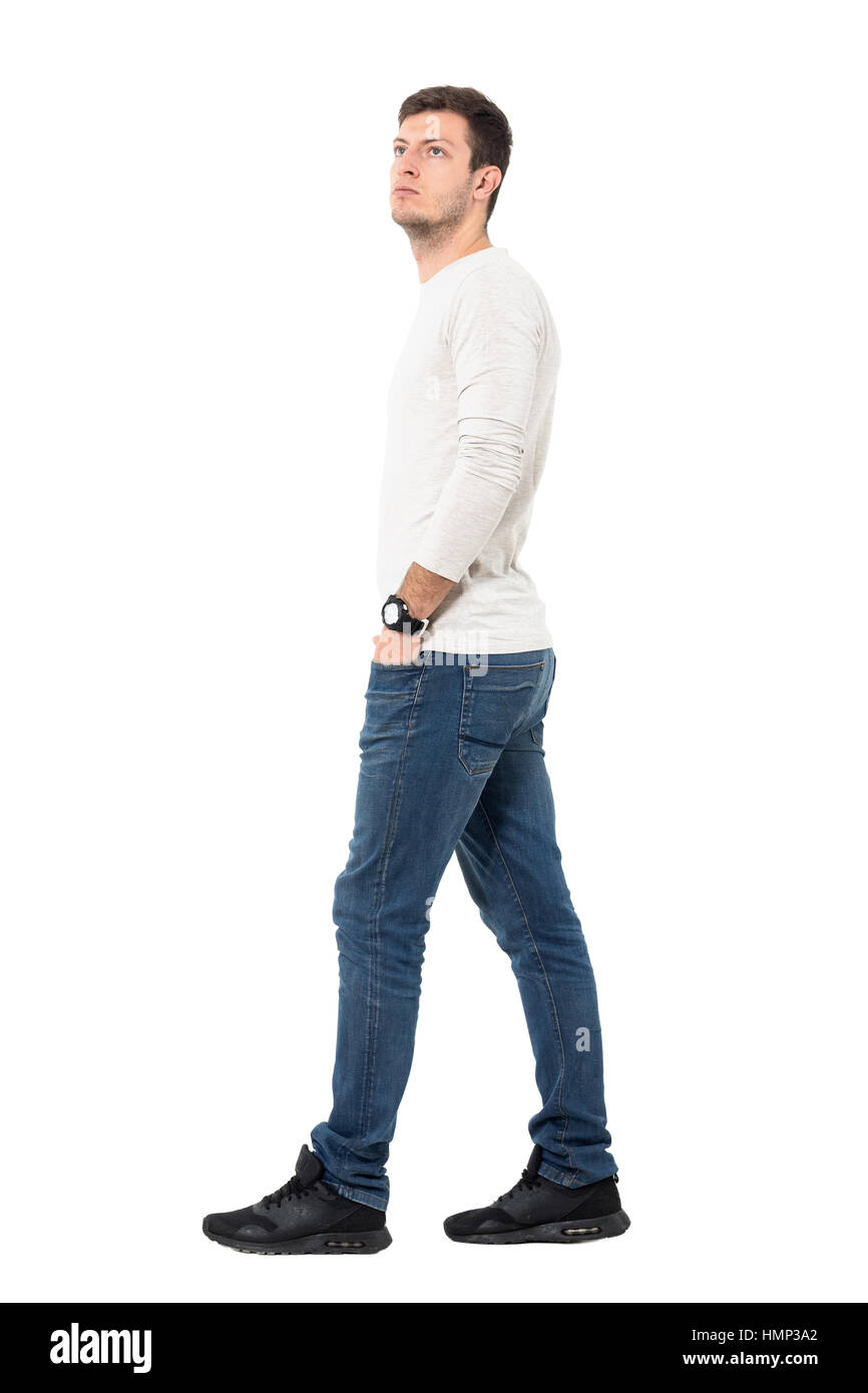 Side view of young relaxed casual man walking with hands in pockets looking up. Full body length portrait isolated over white studio background. Stock Photo