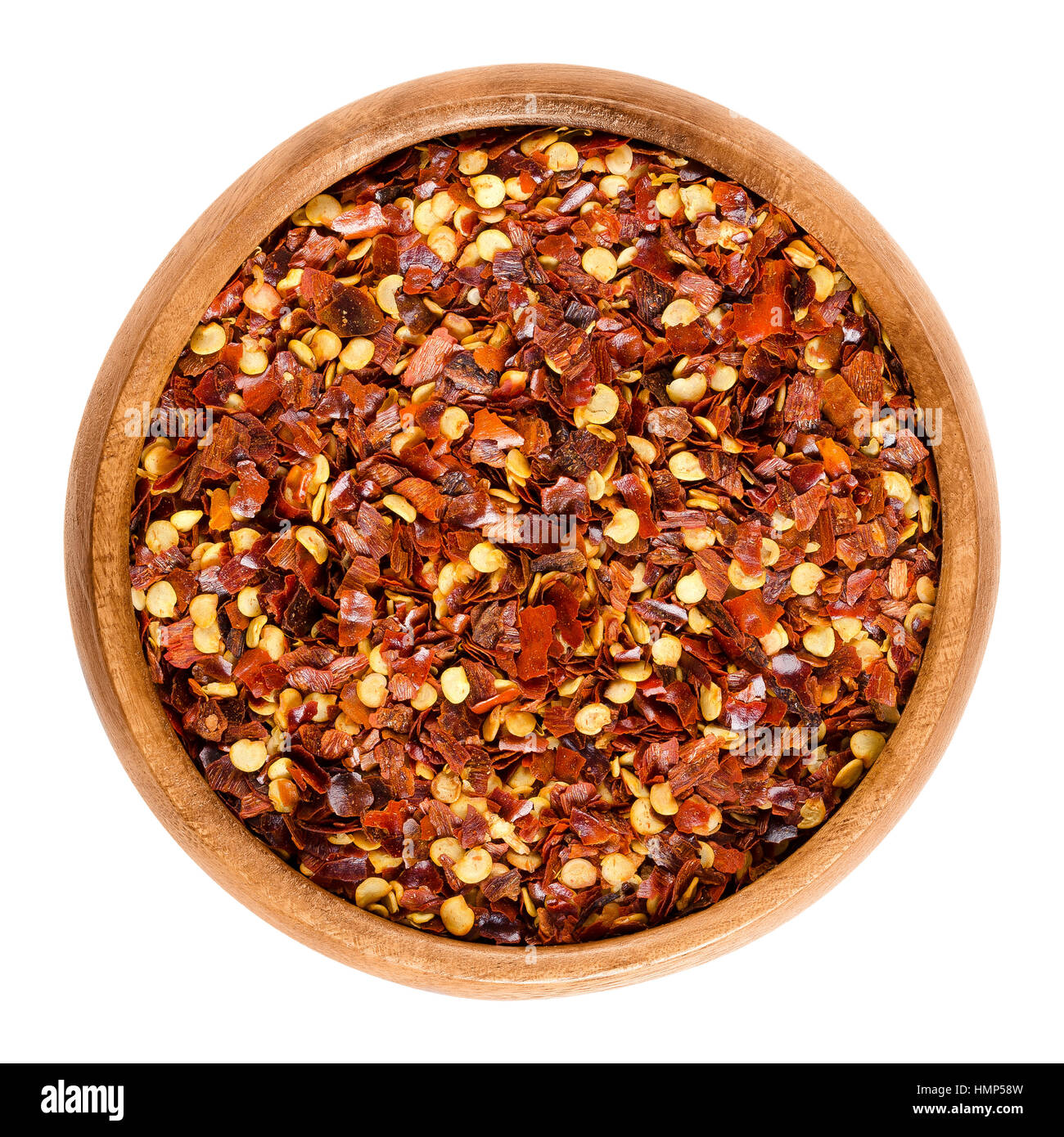 Dried chili pepper flakes in wooden bowl. Dried and crushed fruits of Capsicum frutescens, used as hot spice and for tabasco sauce. Isolated macro foo Stock Photo