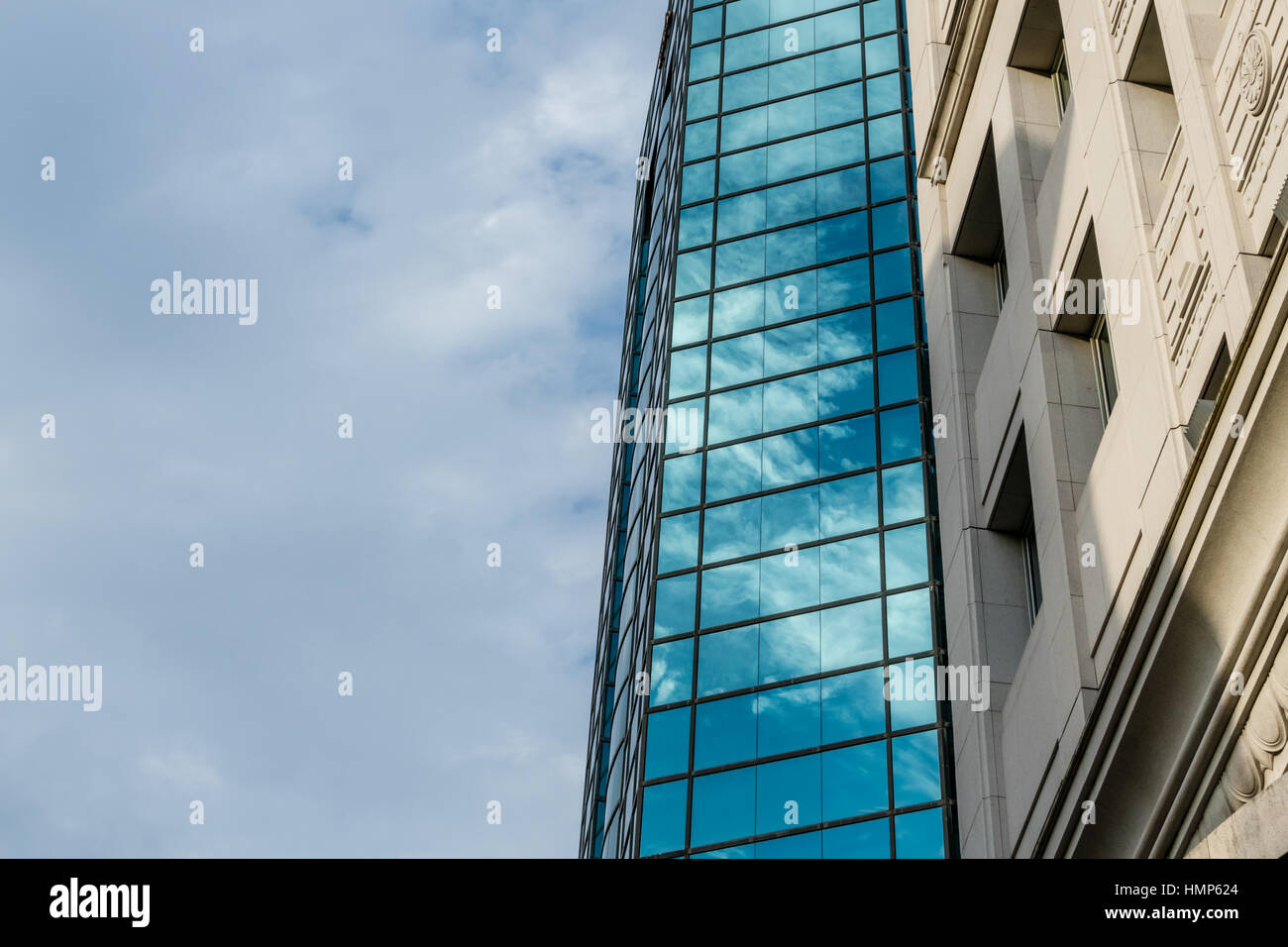 Modern glass building reflecting clouds and sky next to old style building Stock Photo