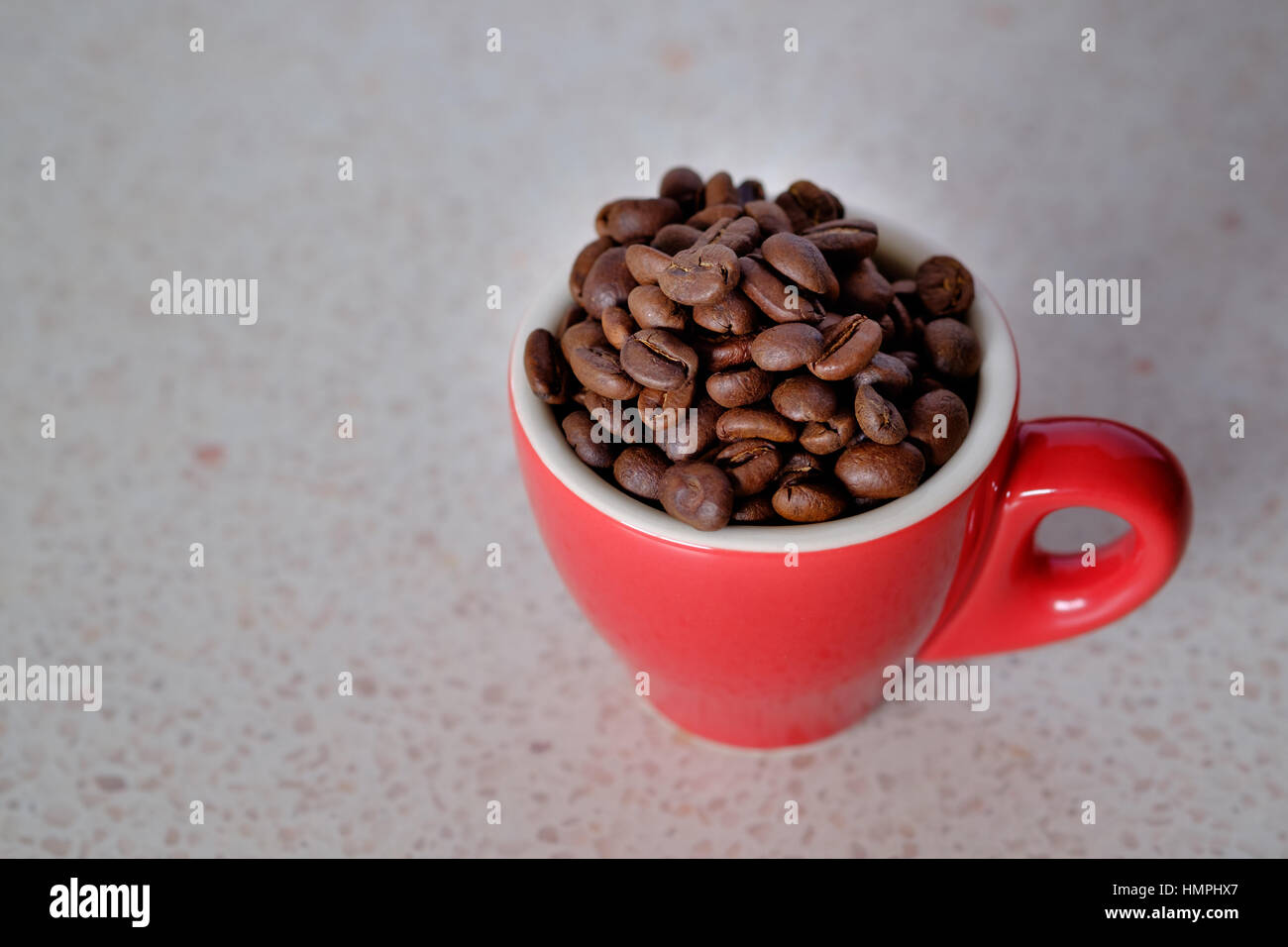 Coffee beans in a red espresso cup on a flecked bench top Stock Photo