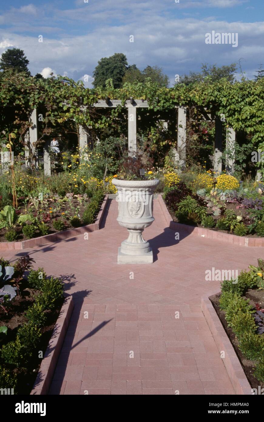 Glimpse of a garden with path ways, flower beds, oramental vase and pergola. Stock Photo