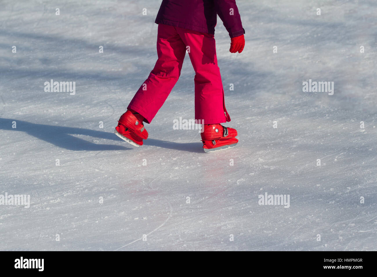 Side view close up of a child in red clothing and iceskates skating on