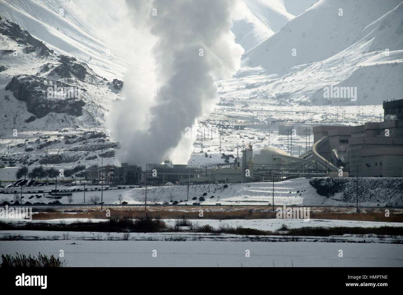 Smoke spewing out of a smokestack and hole from a copper smelting plant with a mountain behind it in Utah. Stock Photo