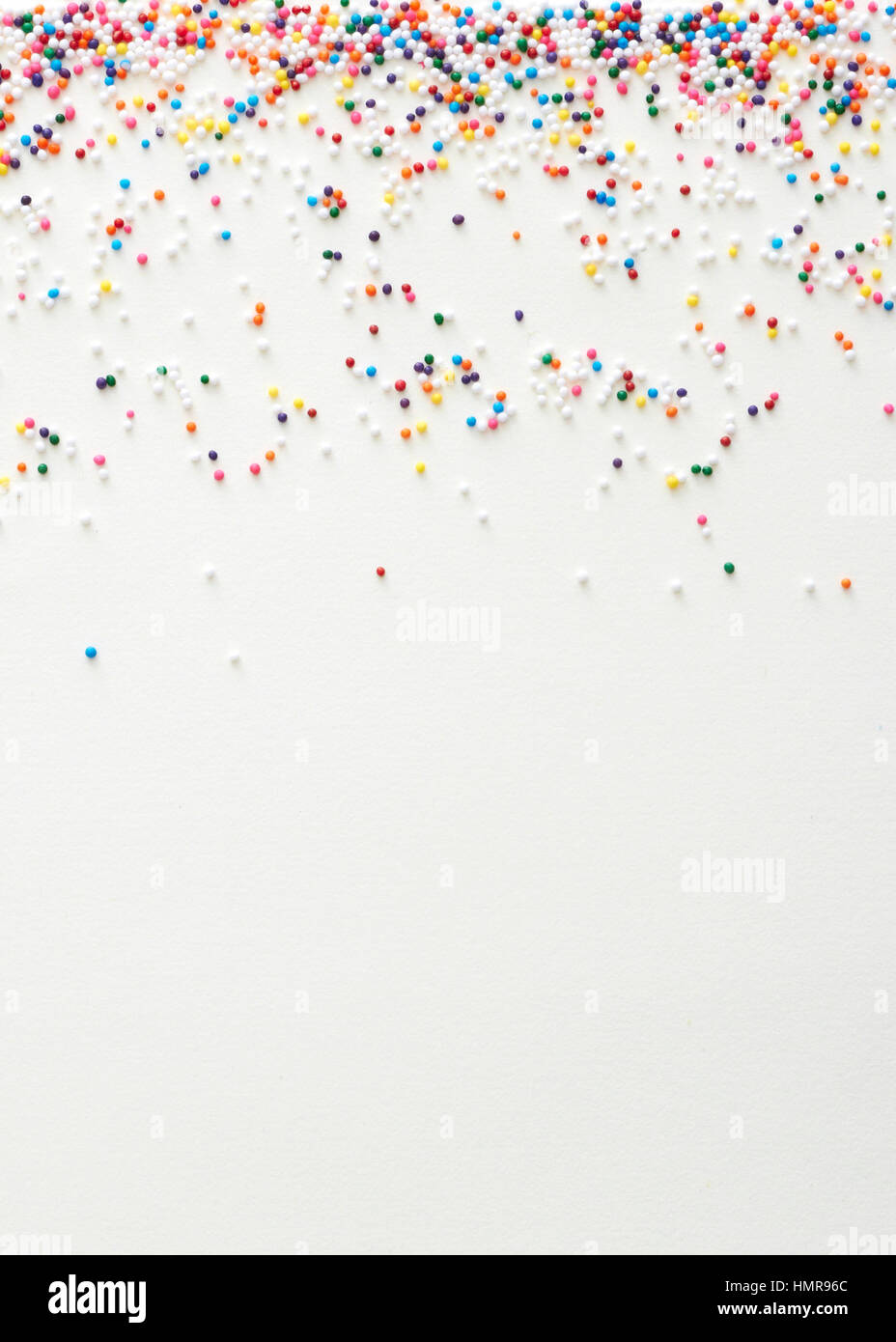 Multi colored nonpareil sprinkles placed as an upper border on a cream paper surface Stock Photo