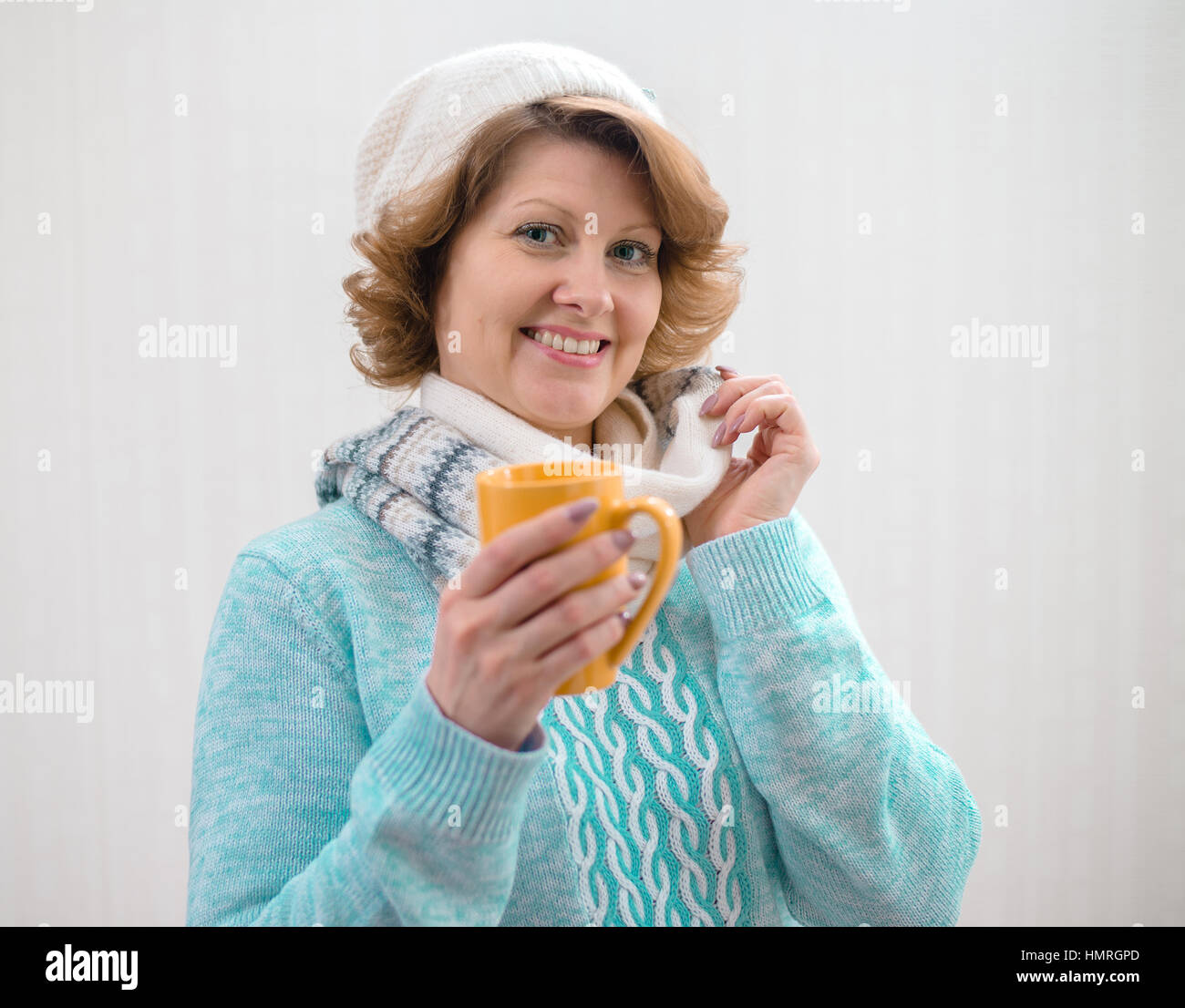 woman in sweater, hat and scarf holding yellow cup of tea Stock Photo