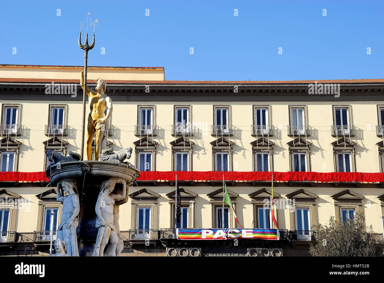 Naples, Italy. Piazza Municipio square. Palazzo San Giacomo, Naples Town Hall with the Peace flag and the seventeenth-century fountain of Neptune was built by the will of the Count Olivares, Enrique de Guzmán, on the direction of Domenico Fontana and with the collaboration of Michelangelo Naccherino, Angelo Landi and Pietro Bernini. Stock Photo