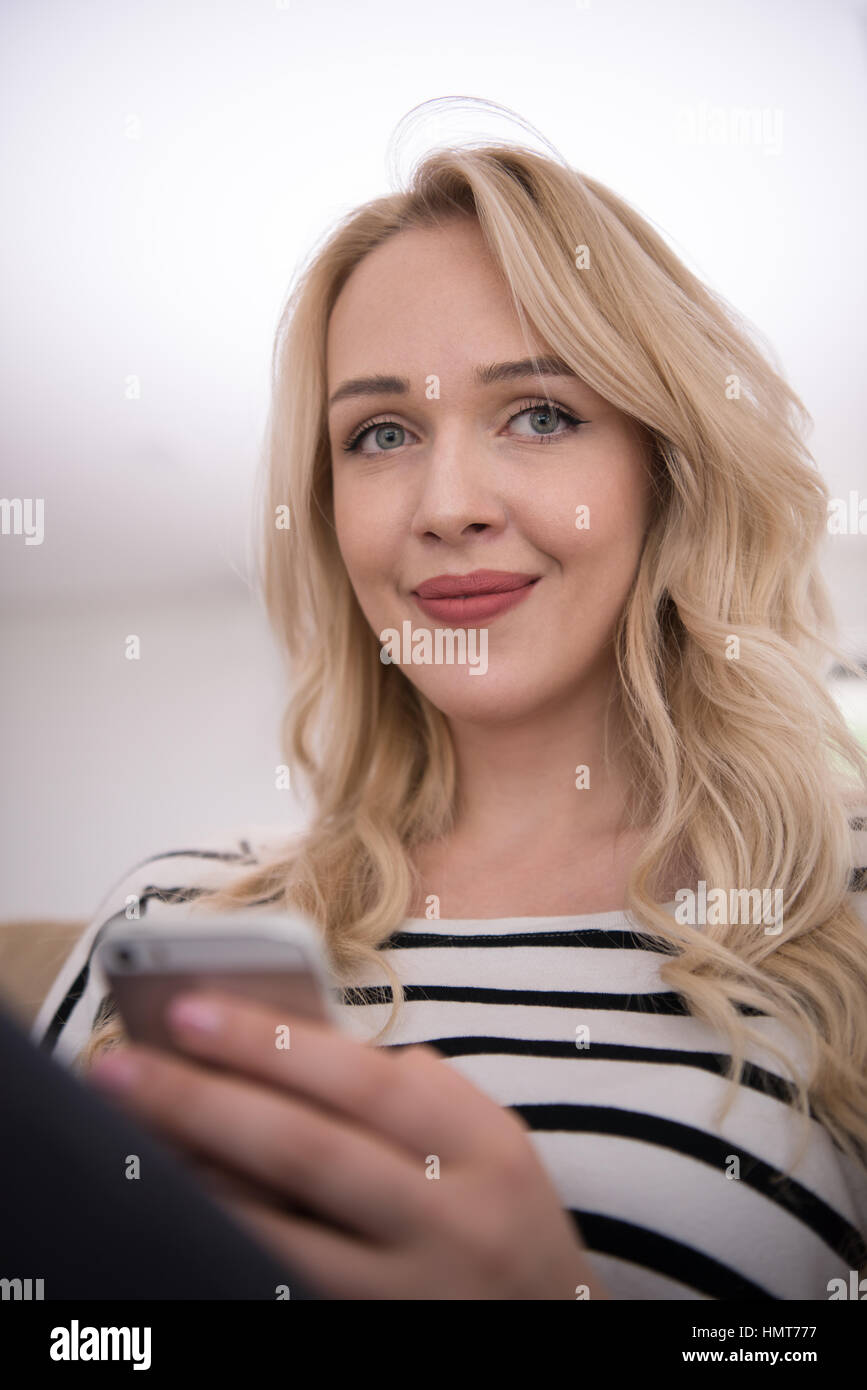 young happy woman sitting on sofa with mobile phone at luxury home ...