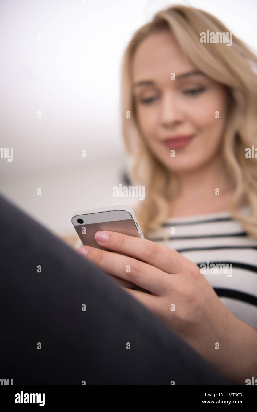 young happy woman sitting on sofa with mobile phone at luxury home ...