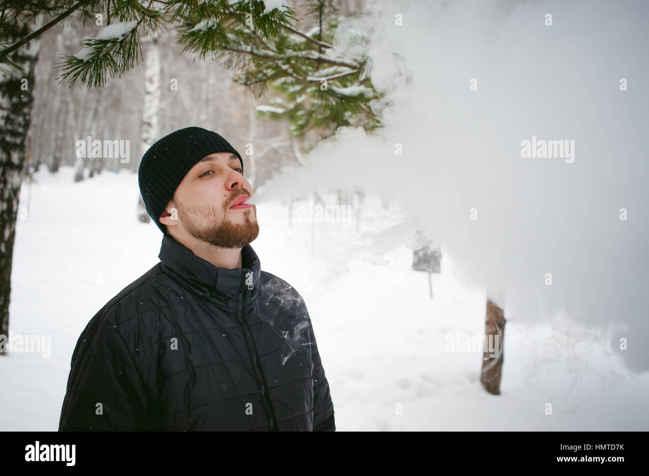 a young man with a beard, smokes an electronic cigarette, outdoors in ...