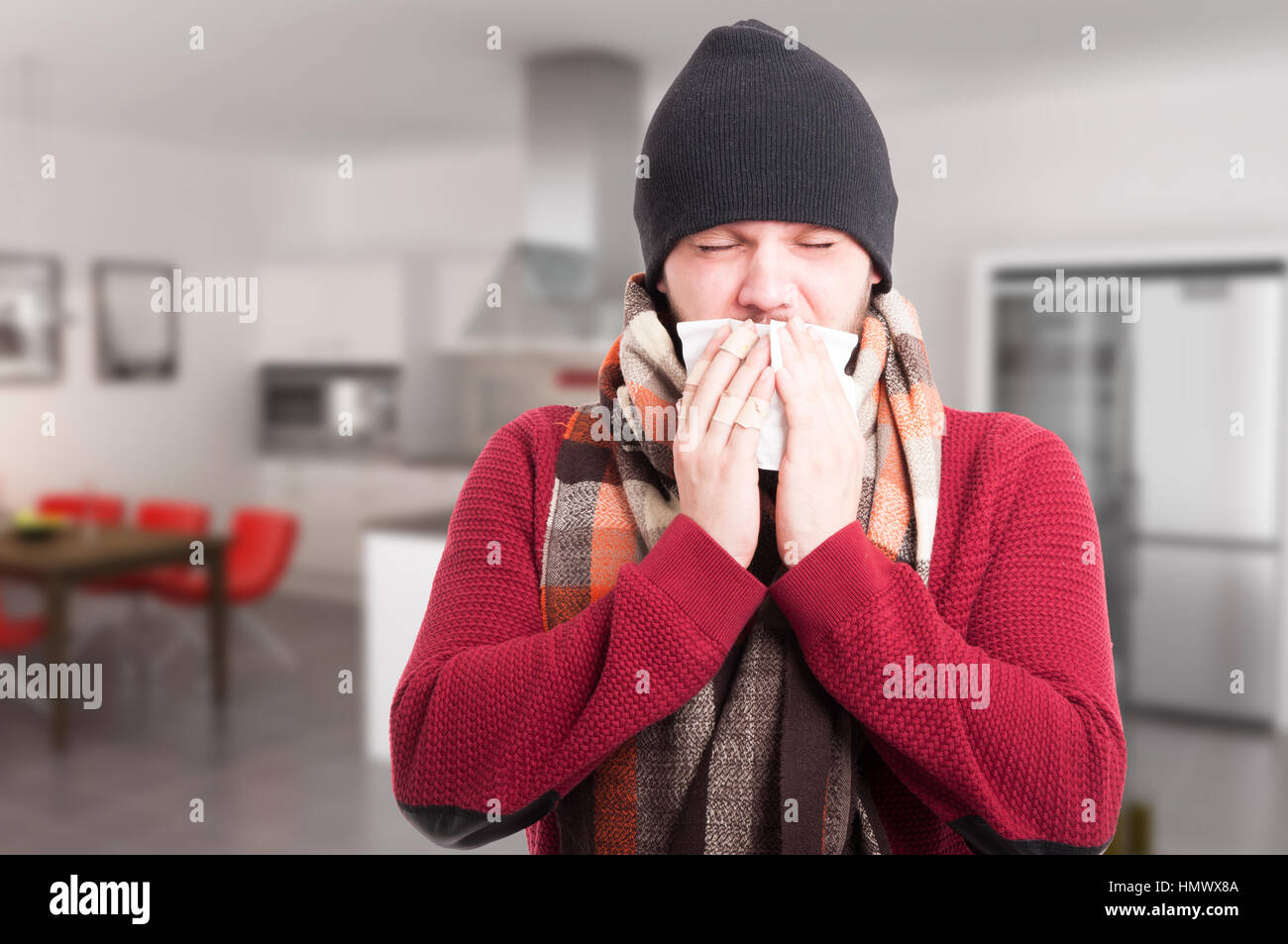 Portrait of ill man with sore throat sneezing in a napkin inside the