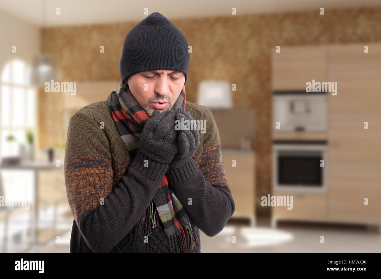 Young man feeling very cold and warming hands with his breath indoors with copyspace Stock Photo