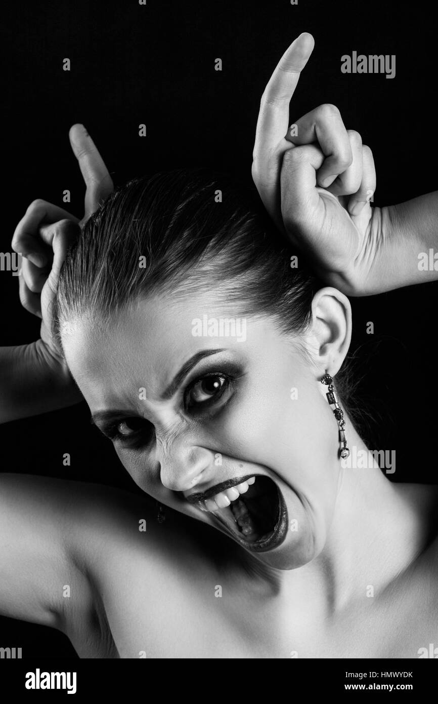 fun luxury woman making devil horns screaming on black background monochrome Stock Photo