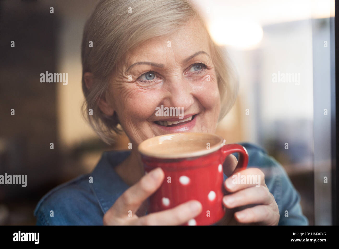 Senior woman at the window holding a cup of coffee Stock Photo