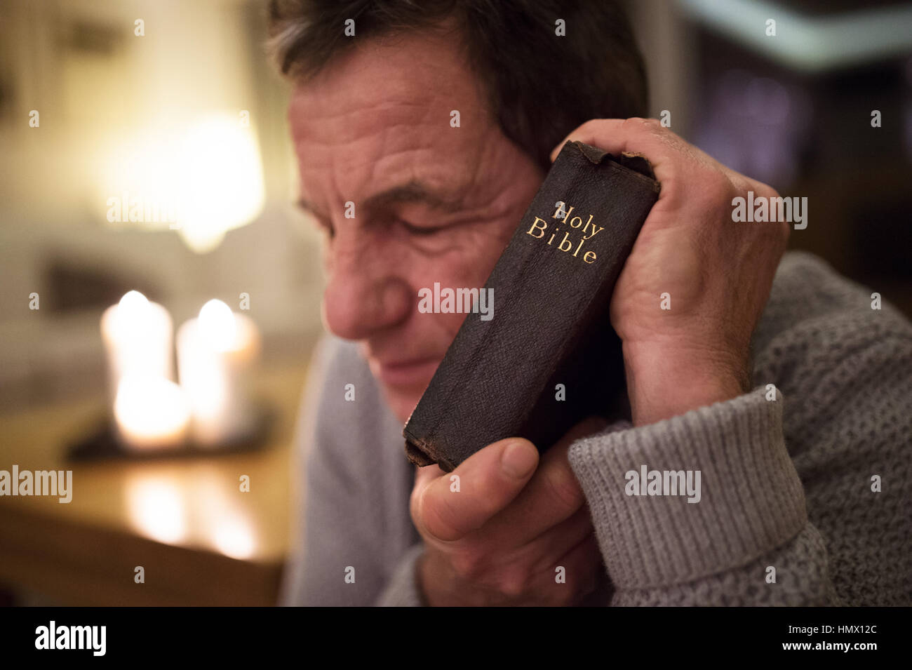 Senior man praying, holding Bible in his hands, eyes closed. Stock Photo