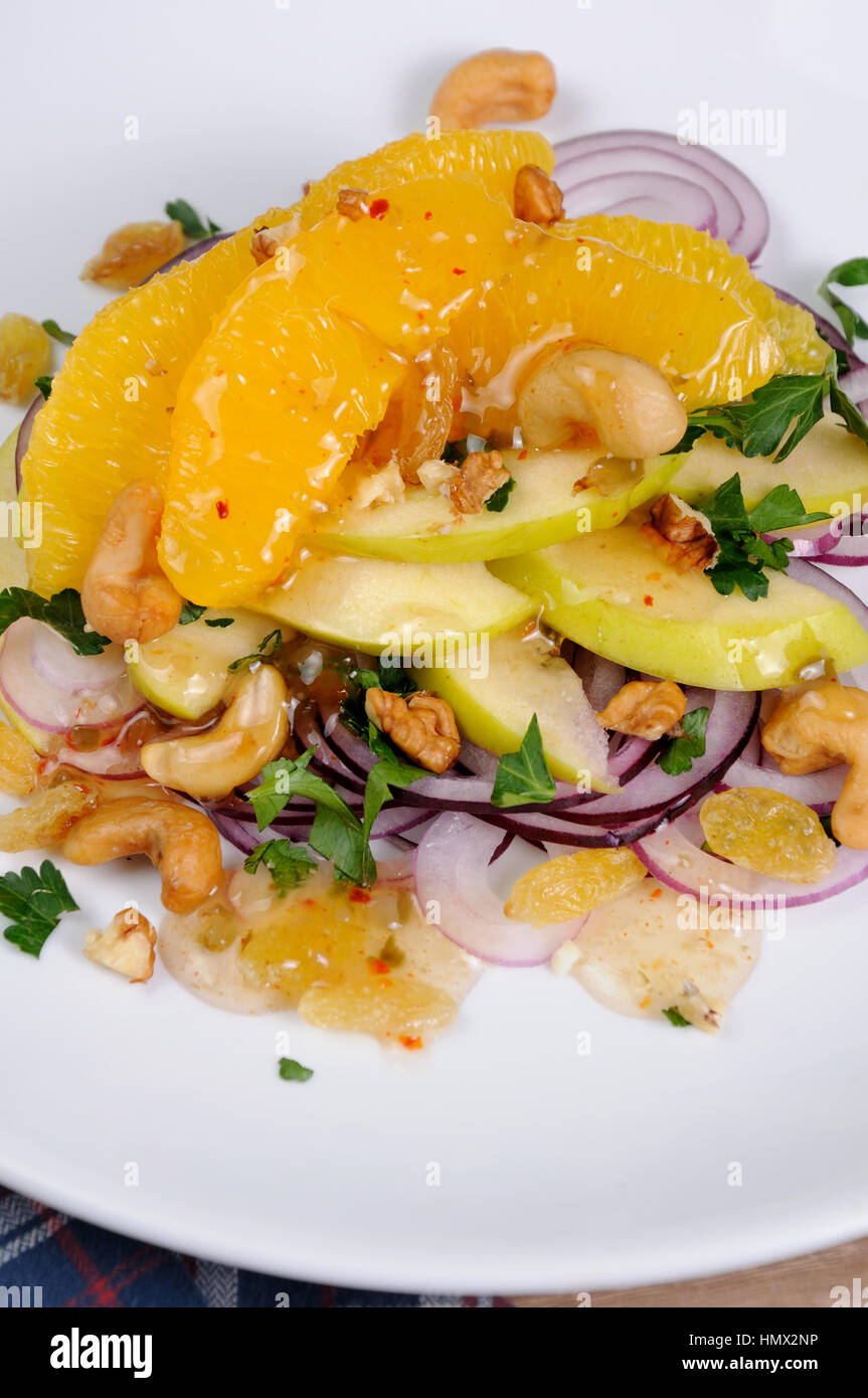 Salad with slices of orange, apple, blue onion, raisin, nuts, cashew nuts, herbs and honey sauce Stock Photo