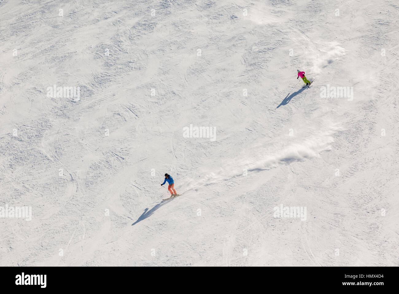 Two skiers on a steep black ski run with trails of snow dust behind them. Stock Photo