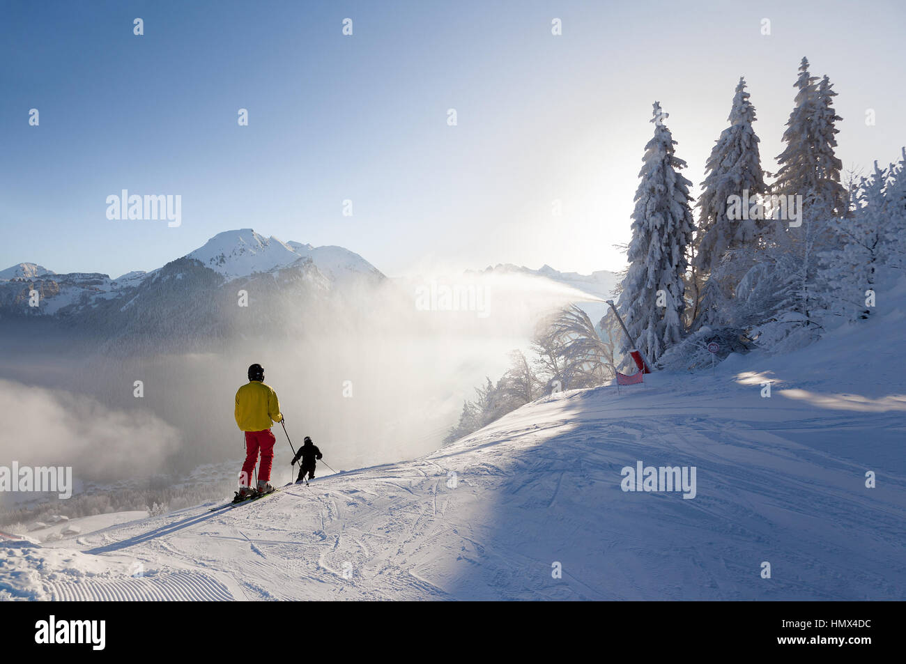 Skiers set off down a piste in the Morzine resort, part of the Portes du Soleil ski area. A snow lance can be seen spraying snow from the side of the  Stock Photo