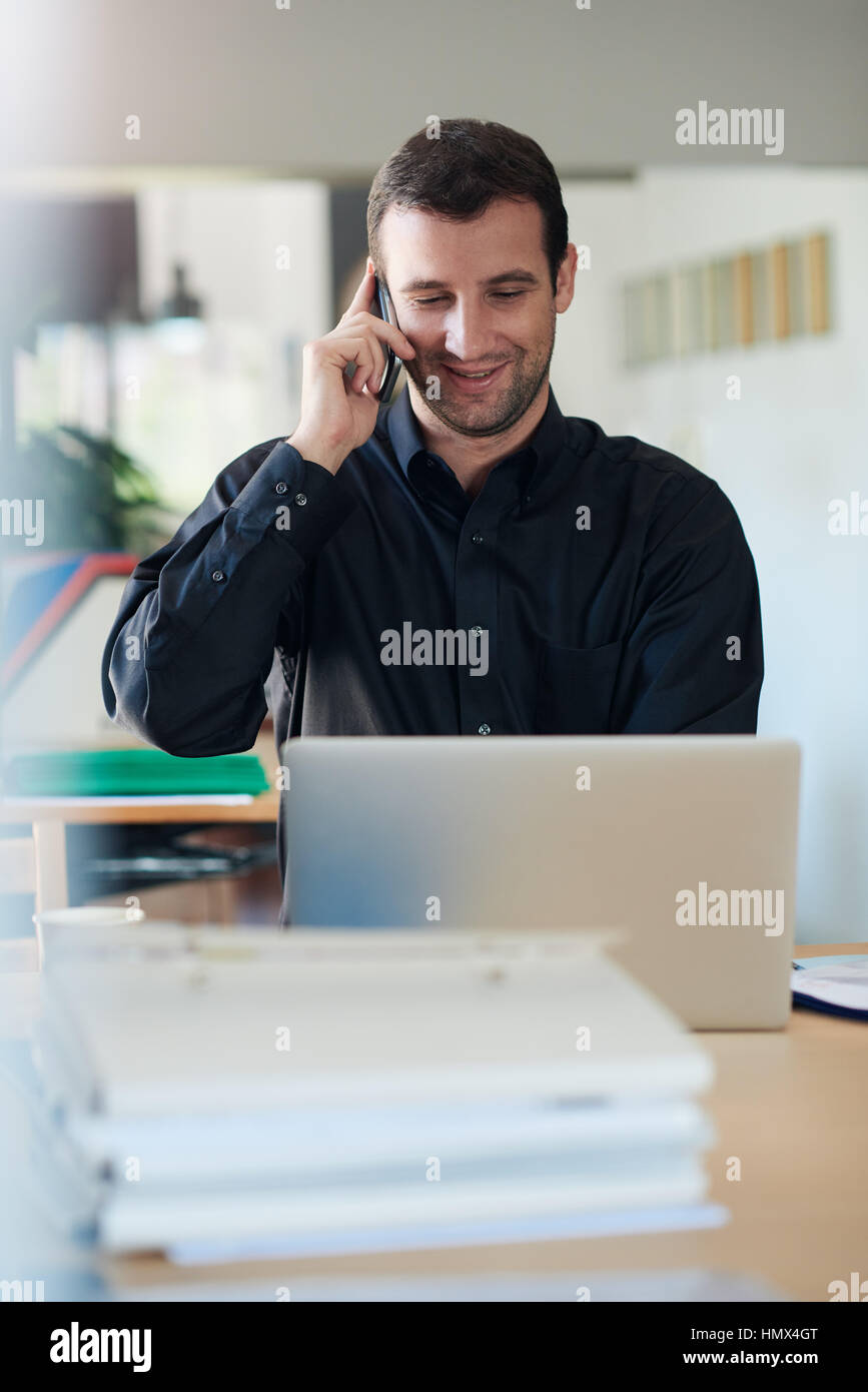 Smiling businessman using a laptop and talking on the phone Stock Photo