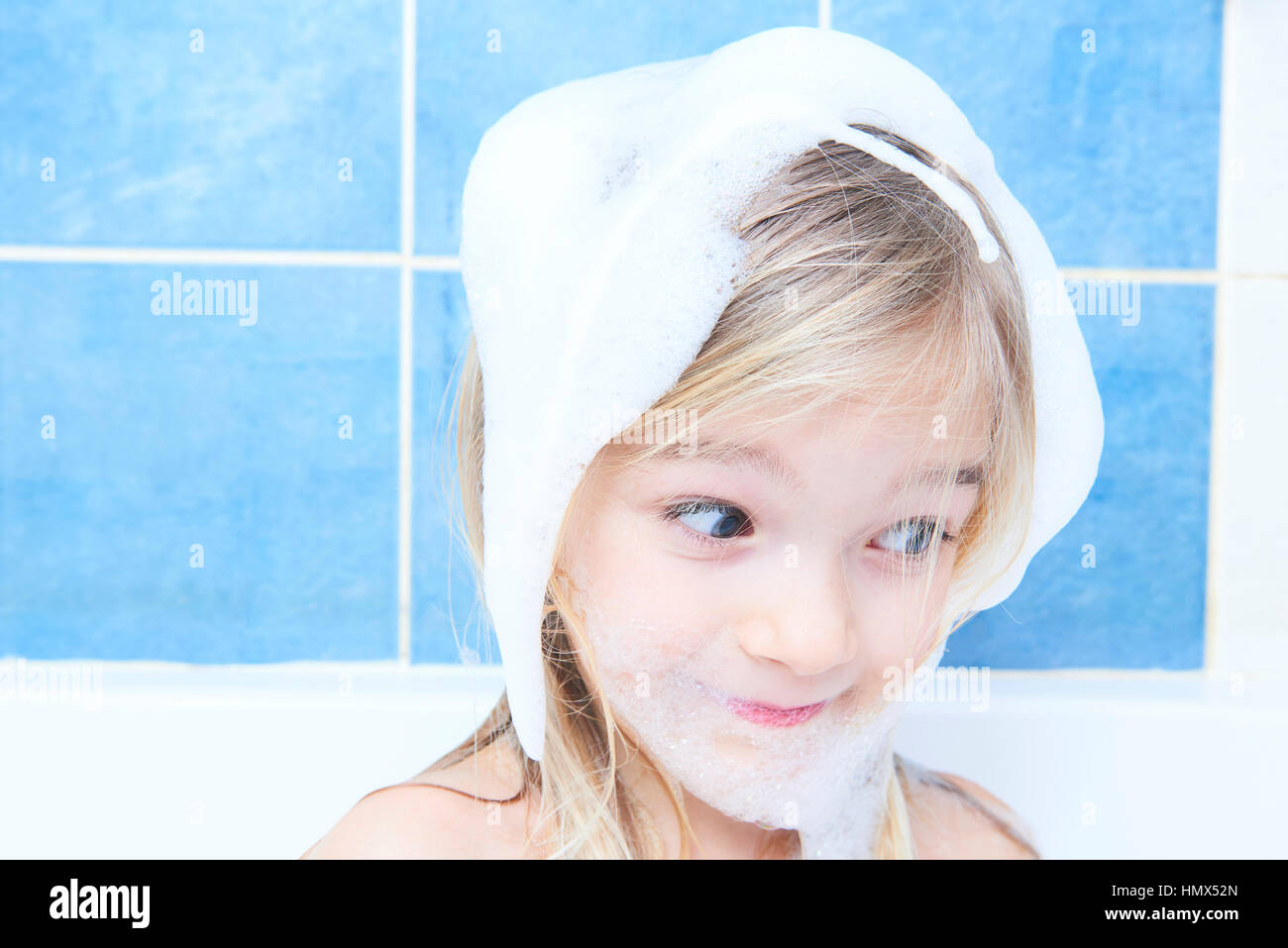 Adorable child blond girl with soap suds on hair taking bath. Closeup