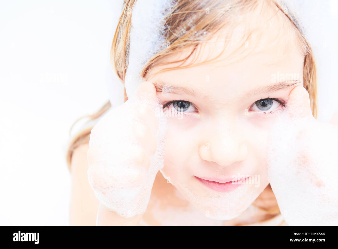 Adorable child blond girl with soap suds on hair taking bath. Closeup